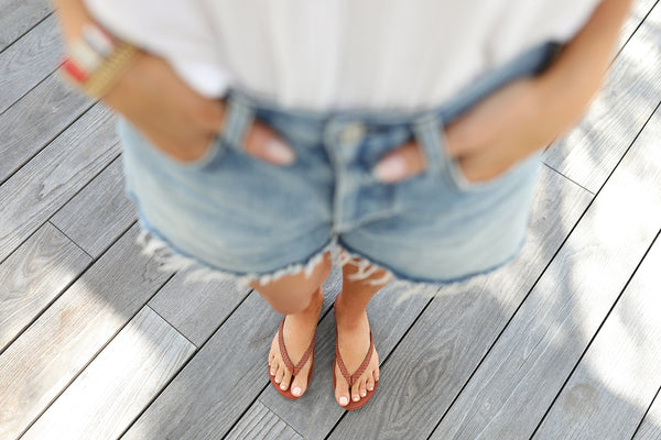 Woman wearing Seabird Woven leather flip flop sandals in tan with jean shorts.