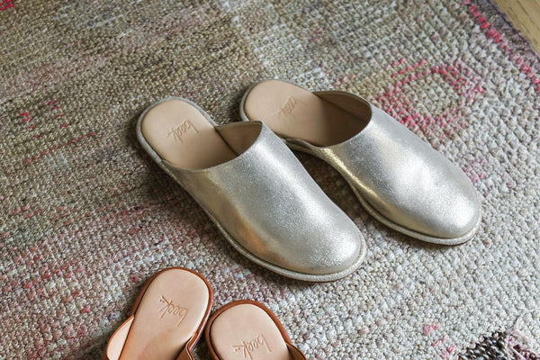 Seagull leather mules in gold on rug.