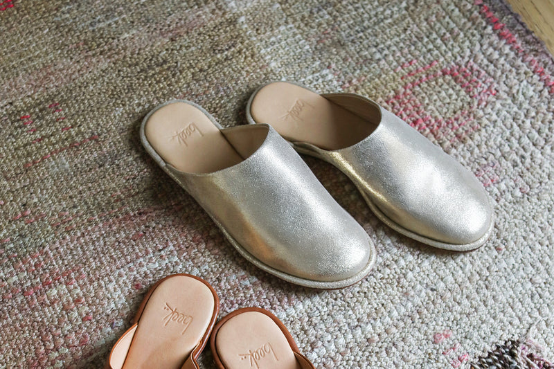 Seagull leather mules in gold on rug.