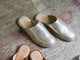 Seagull leather mules in gold on rug.