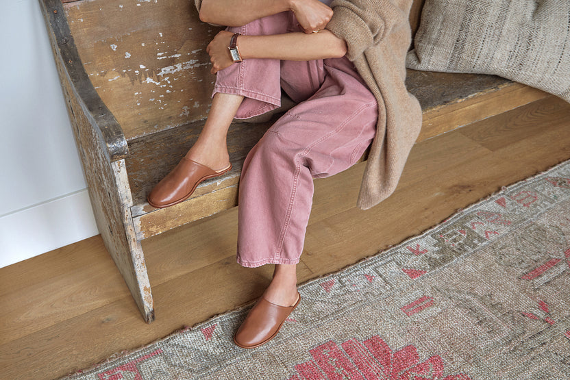 Woman wearing Seagull leather mule in tan with pink jeans and sweater, sitting on bench.