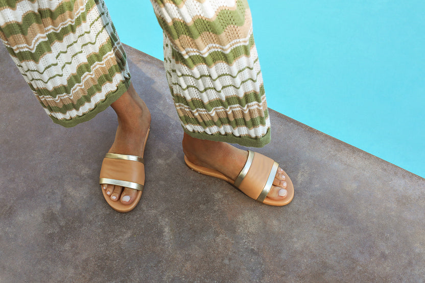 Woman wearing Shorebird leather slide sandal in beach/gold with patterned knit pants