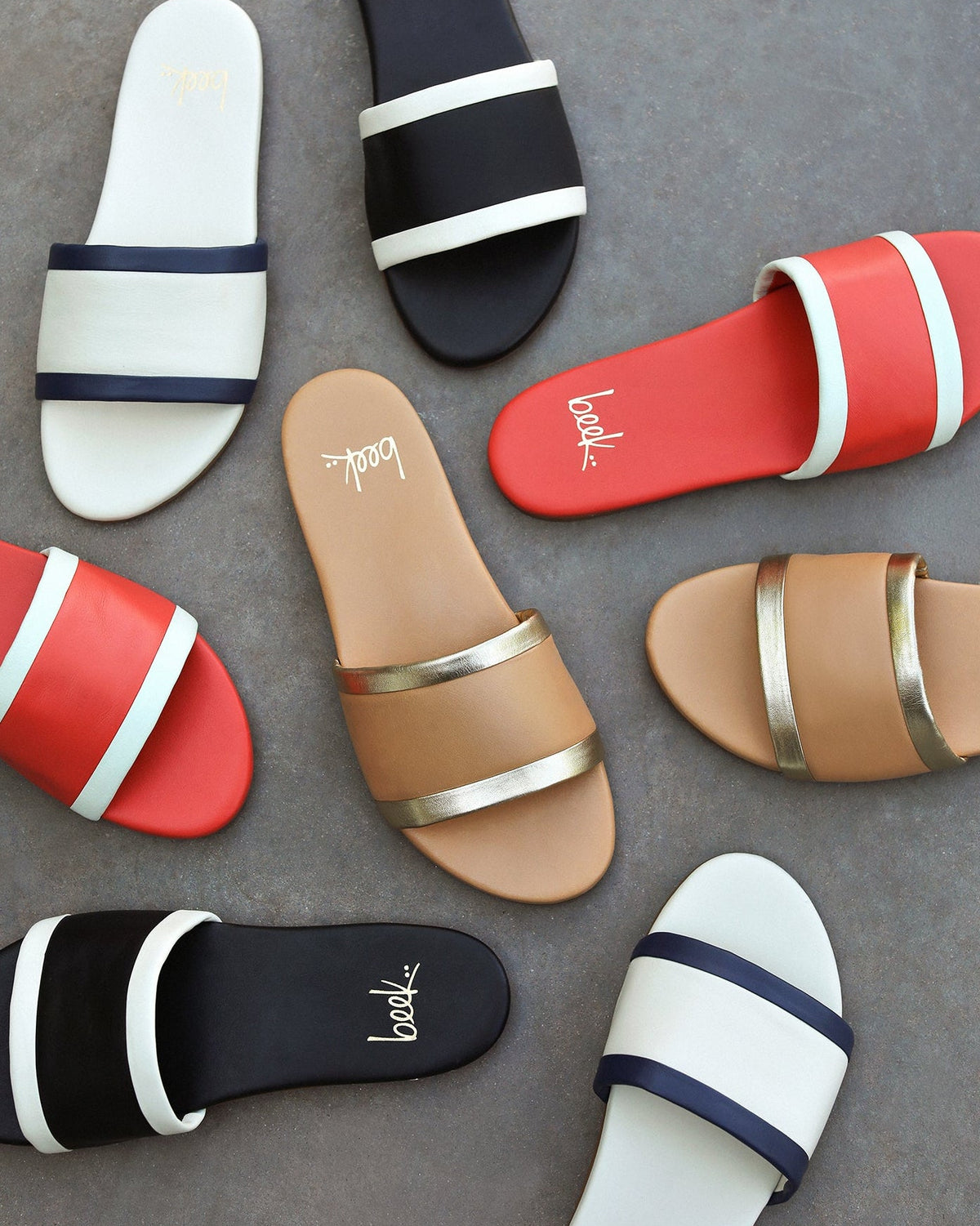 Group shot of Shorebird leather slide sandal in vanilla/navy, black/vanilla, tomato/vanilla, and beach/gold.