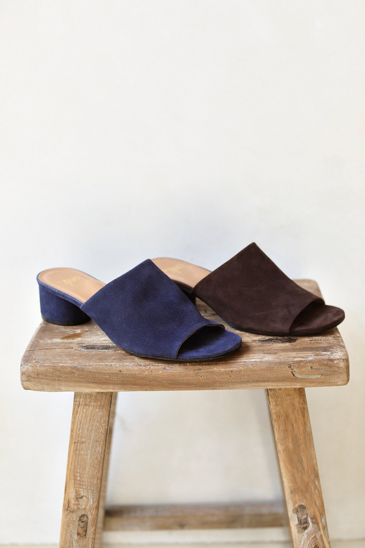 Group shot of Stilt suede heeled sandals in navy and chocolate on a stool