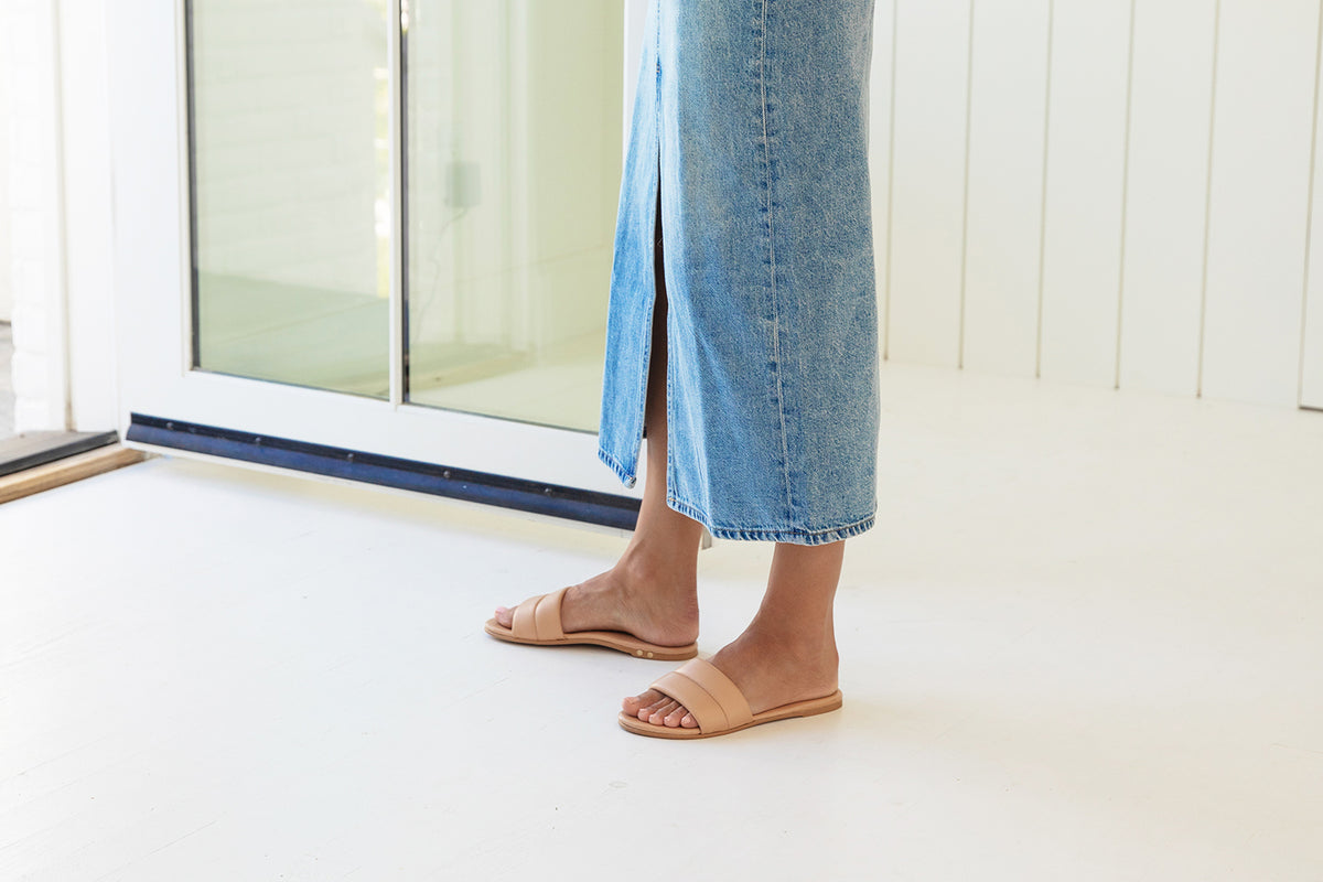 Woman wearing Sugarbird leather slide sandals in beach with denim skirt
