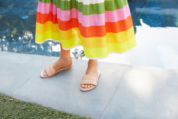 Woman wearing Sugarbird leather slide sandals in beach with colorful striped dress