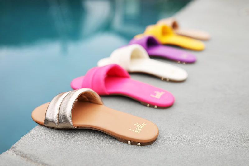 Group shot of Sugarbird leather slide sandals in gold/honey, azalea, eggshell, iris, sunflower, and beach