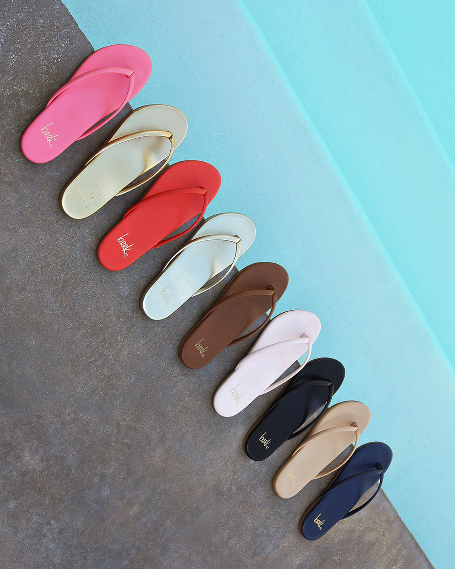 Group shot of Sunbeam leather flip flop sandals in peony, oro, tomato, platinum, tan, blossom, black, beach, navy
