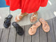 Woman wearing Sungem leather sandals in gold with red dress, standing next to Sungem sandals in black and beach.
