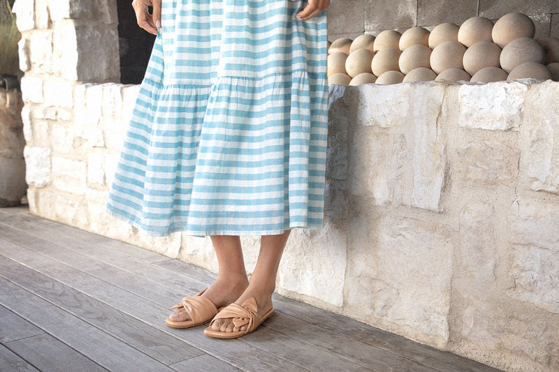 Woman wearing Sweetbird leather slide sandals in beach with blue and white striped dress