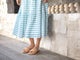 Woman wearing Sweetbird leather slide sandals in beach with blue and white striped dress