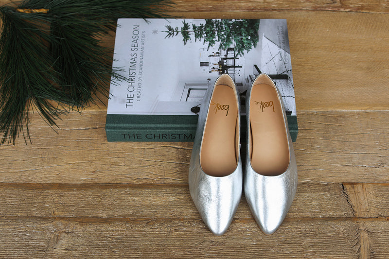 Swoop leather ballet shoes in silver propped on a Christmas book.