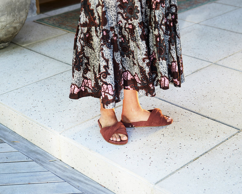 Woman wearing Tesia suede slide sandal in fig with skirt