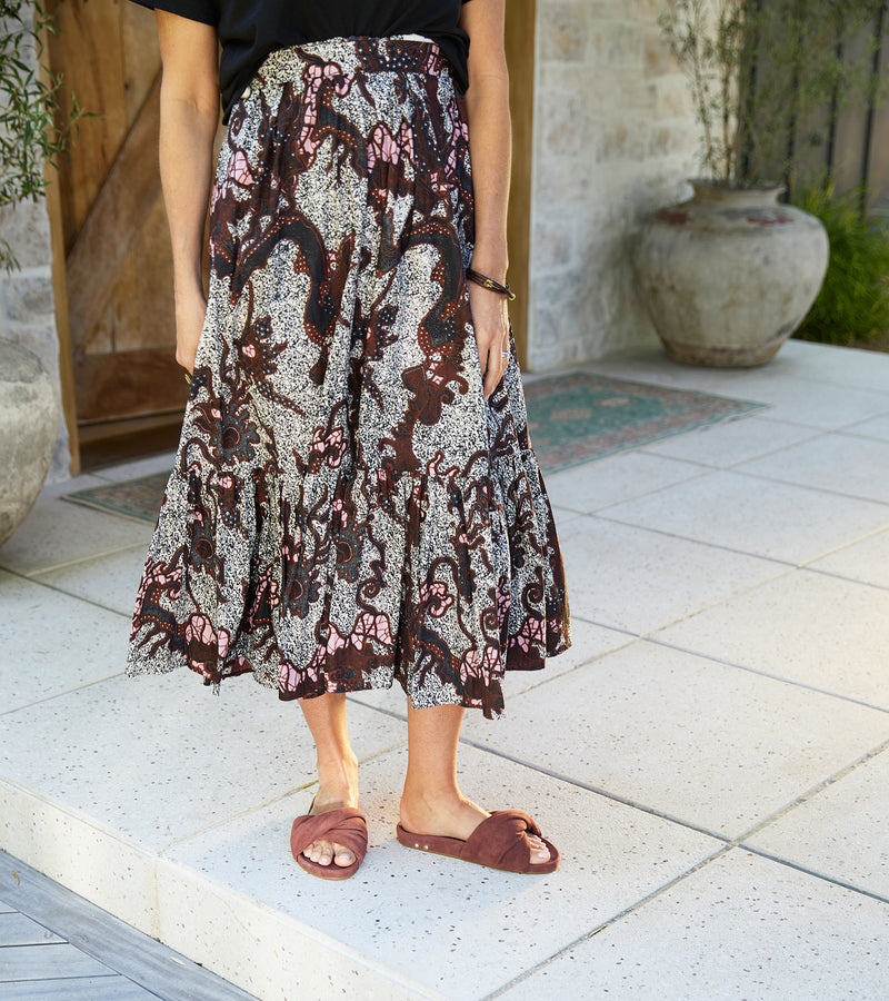 Woman wearing Tesia suede slide sandal in fig with patterned skirt