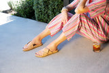 Woman wearing Tori leather sandals in beach with striped jumpsuit.