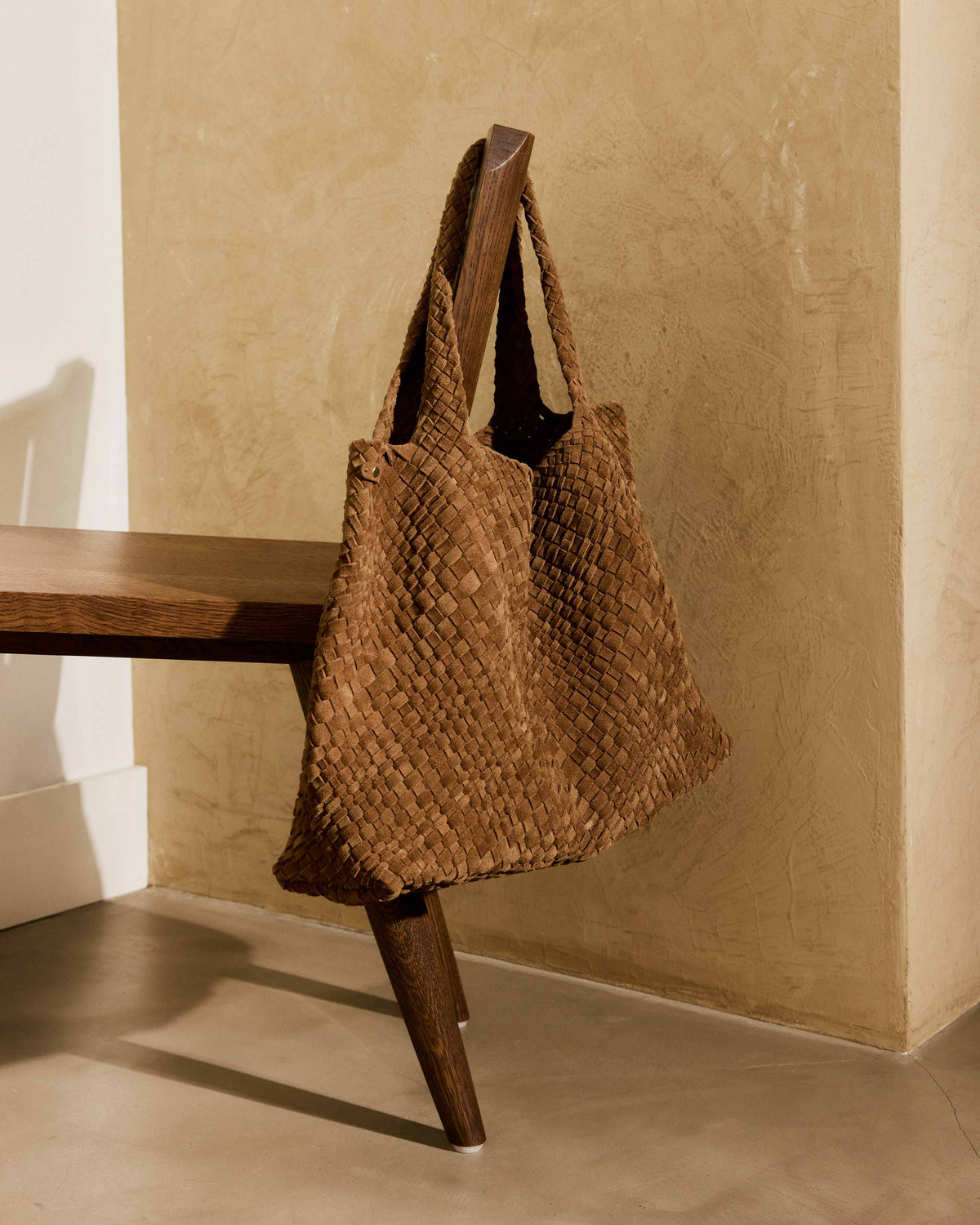 Willet suede woven tote bag in chestnut hangs from a chair