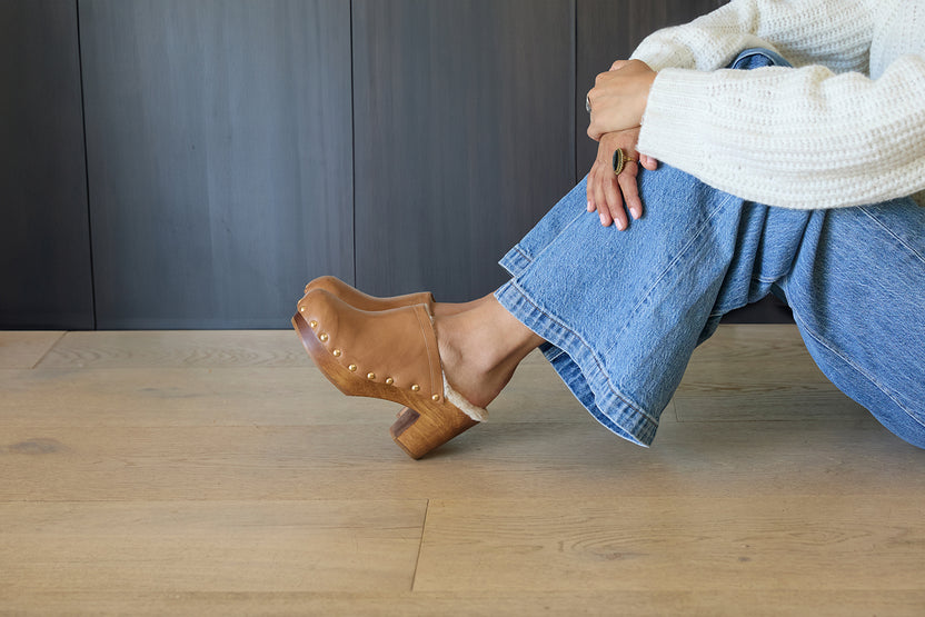 Woman wearing Woodpecker Shearling clogs in saddle with jeans and sweater