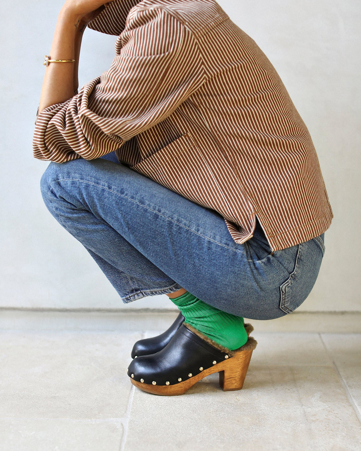 Woman wearing Woodpecker Shearling clogs in black with green socks, jeans, checkered jacket