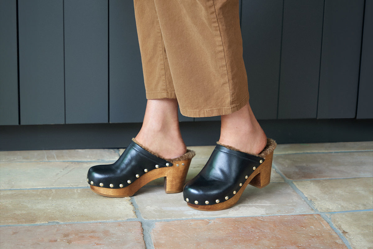 Woman wearing Woodpecker Shearling clogs in black with brown pants